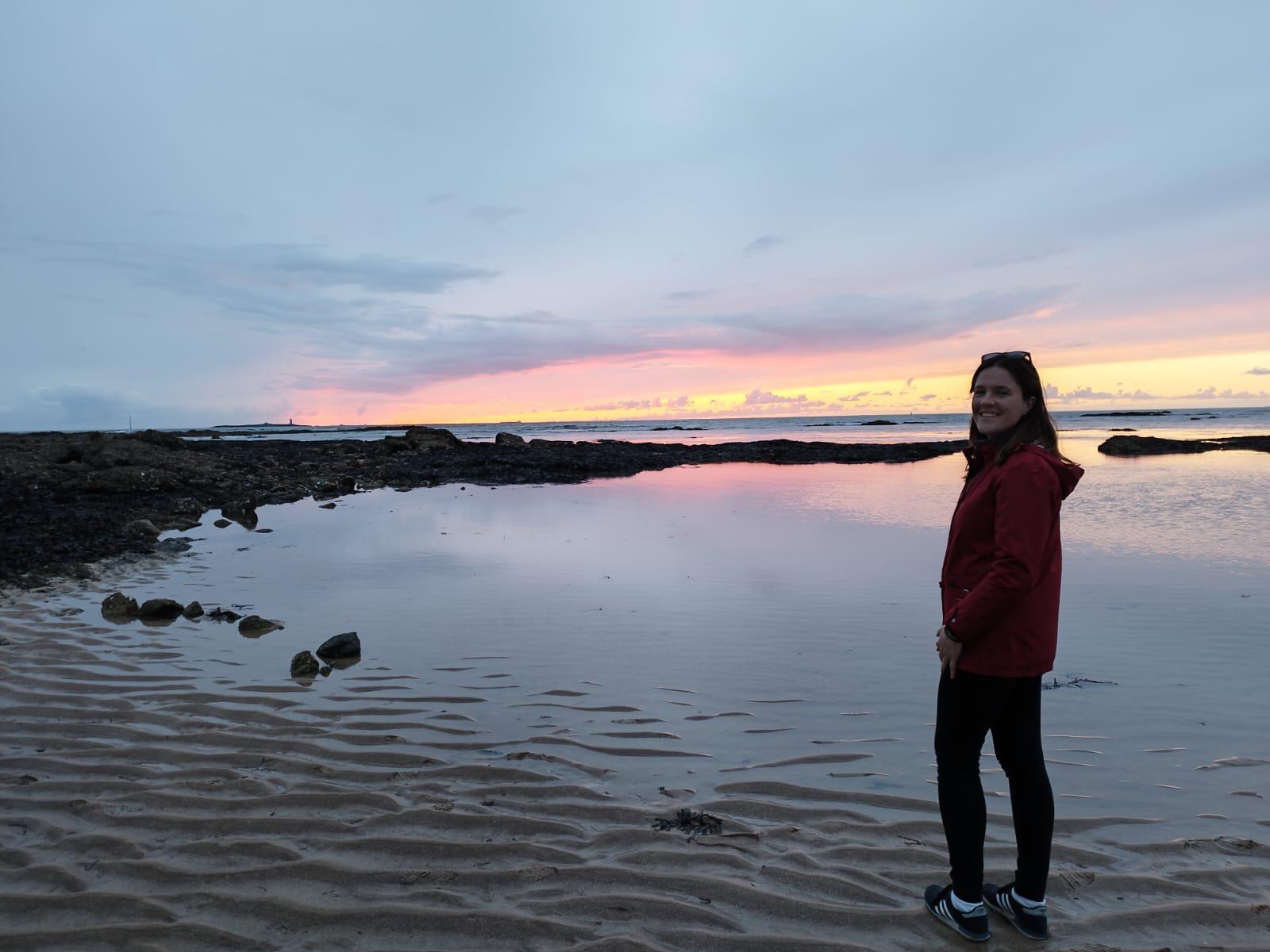 Chloé Logeais souriante, regardant vers le formulaire, avec un coucher de soleil en arrière-plan, symbolisant un accueil chaleureux et professionnel.