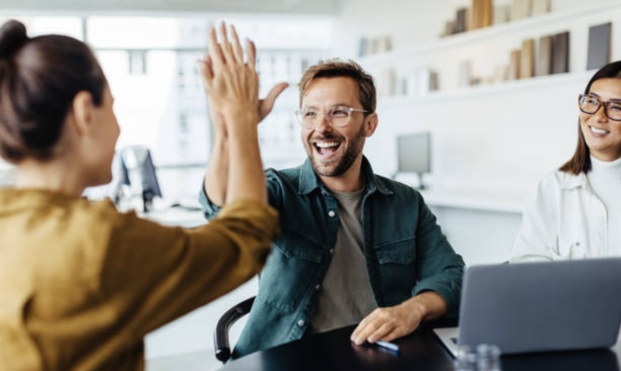 Groupe de professionnels autour d’un bureau célébrant leur succès, symbolisant la confiance acquise grâce au coaching en anglais.